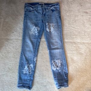 Free People stretch skinny jeans with a bleached, white flower pattern.